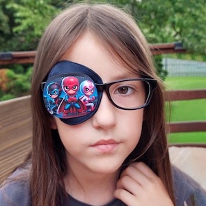 May include: A navy blue eye patch with a superhero design, worn over the left eye. The patch features three cartoon superheroes in red, blue, and pink. The person is also wearing black eyeglasses.