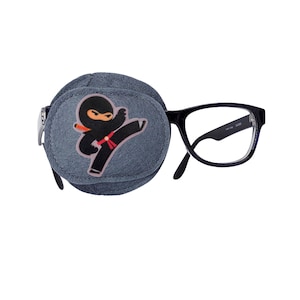 Puede incluir: Un parche para el ojo gris con un diseño de ninja de dibujos animados unido a gafas con montura negra.