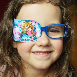 May include: A young girl wearing blue glasses with a blue and white eye patch featuring a cartoon image of two princesses. The eye patch has a white snowflake pattern.