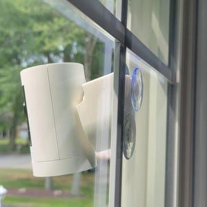 May include: A white security camera mounted on a window with suction cups.