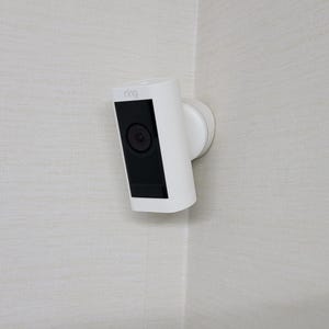 May include: A white security camera mounted on a wall with a black lens.