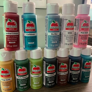 May include: A collection of 10 acrylic craft paint bottles in various colors, including cardinal crimson, caribbean, sky blue, white, pink parfait, kings gold, kelly green, limeade, pavement, nutmeg brown, admiral blue, and laguna. Each bottle is 2 fl oz (59 ml) and features the Apple Barrel brand logo.