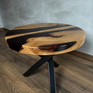 Op de afbeelding: Ronde houten tafel met een zwart epoxyhars blad en een zwart metalen X-vormig onderstel.