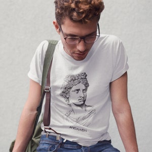 May include: A white t-shirt with a black and white illustration of a bust of a person with the text "ANACAOA" printed on the bottom.