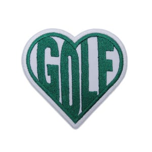Può includere: Toppa a forma di cuore con la scritta "GOLF" ricamata in verde su sfondo bianco. La toppa ha un bordo bianco ed è progettata per essere cucita o stirata su abbigliamento o accessori.