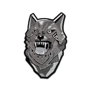May include: An embroidered patch featuring a stylized wolf head in shades of gray, black, and white. The wolf is depicted with an open mouth, bared teeth, and geometric patterns on its face, all outlined with a thick black border for definition.