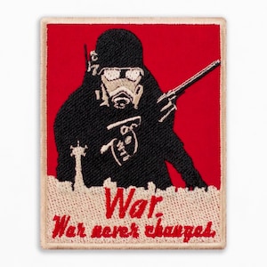 Può includere: Toppa ricamata con una silhouette nera di un soldato con maschera antigas e fucile su sfondo rosso. La toppa include le parole "War. War never changes" in un font stilizzato, con un bordo beige.