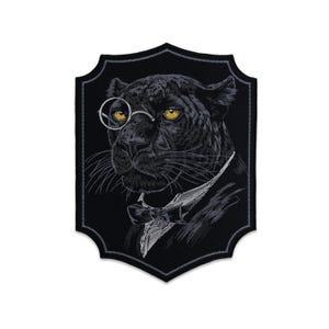 May include: A black shield-shaped embroidered patch featuring a panther wearing a monocle and a bowtie. The panther has bright yellow eyes and is depicted in shades of black and grey thread against a solid black background with a grey border.