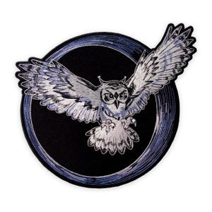 May include: Embroidered patch featuring a detailed owl with outstretched wings, in shades of gray and white, set against a black circular background with a blue border. The owl's eyes are focused, and its talons are visible.