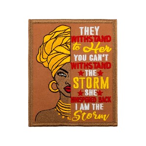 Könnte beinhalten: Gestickter Aufnäher mit einem Porträt einer Frau mit gelbem Kopftuch und Goldschmuck. Der Text auf dem Aufnäher lautet: „They withstand to Her, You can't withstand the storm, She whispered back, I am the storm.“