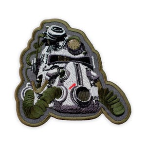 May include: Embroidered patch featuring a detailed image of a vintage diving helmet. The patch has a gray background with a green and brown border. The helmet is white with black, green, and red accents. The design includes hoses and other equipment.
