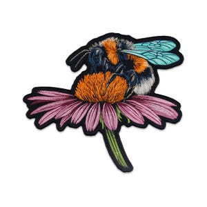 May include: Embroidered patch featuring a detailed bumblebee on a purple coneflower. The bee has orange, black, and white fur with turquoise wings. The flower has pink petals and an orange center, all outlined in black.