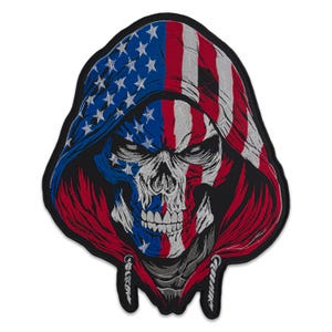 Könnte beinhalten: Gestickter Aufnäher mit einem Totenkopf, der eine Kapuze mit dem Design der amerikanischen Flagge trägt. Der Totenkopf ist mit weißem, blauem und rotem Garn detailliert, und die Kapuze zeigt das Sternen- und Streifenmuster.