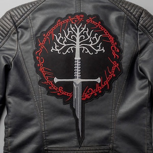 May include: Black leather jacket featuring a large embroidered patch on the back. The patch depicts a white tree, a silver sword, and red script on a black background. The jacket has quilted shoulder detailing.
