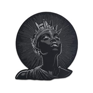 Puede incluir: Un parche bordado circular con una ilustración gráfica en blanco y negro de una persona con una corona de púas. El diseño incluye líneas radiantes detrás de la cabeza y una prenda drapeada, realizado con hilo de alto contraste sobre tela.