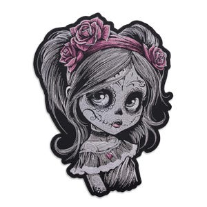 Pode incluir: Patch bordado com uma menina estilizada do Dia dos Mortos com um rosto de caveira de açúcar, adornada com uma faixa de rosas cor-de-rosa. O patch tem uma borda preta e costuras detalhadas, perfeito para jaquetas, bolsas ou outros tecidos.