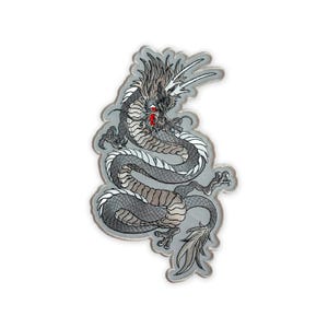 May include: An embroidered patch featuring a serpentine dragon in shades of grey, black, and white. The dragon has a long, winding body with detailed scales, sharp claws, and a prominent red accent near the mouth, finished with a light grey border.
