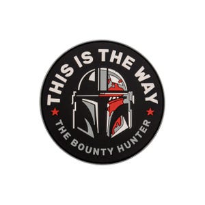 Op de afbeelding: Een ronde, zwarte patch met de tekst "THIS IS THE WAY" in het wit, rond een afbeelding van een Mandalorian helm. De helm is zwart, grijs en rood, met twee rode sterren. De tekst "THE BOUNTY HUNTER" is ook in het wit.