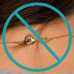 May include: A thin gold chain necklace featuring a lobster claw clasp mechanism. The delicate metal links are connected by a circular jump ring, showcasing the functional closure hardware of the jewelry piece resting against the skin.
