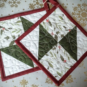 May include: Two quilted pot holders with a white background and green and red floral pattern. The pot holders have a red border.
