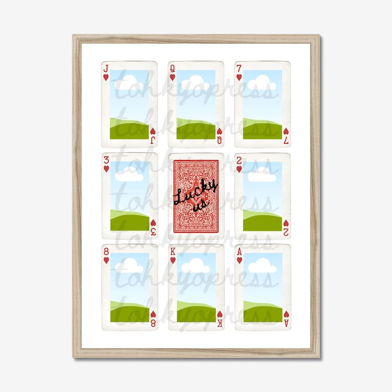 May include: A framed print featuring playing cards with a landscape design. The central card reads "Lucky us" in script. The other cards display hearts and numbers. The artwork is set against a white background.