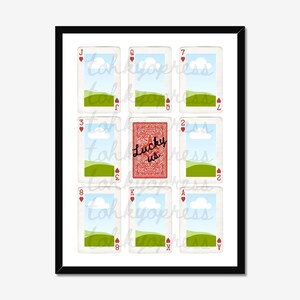 May include: A framed print featuring playing cards. The image includes a red playing card with the text "Lucky us" and other cards with landscape scenes. The cards are arranged in a grid pattern.