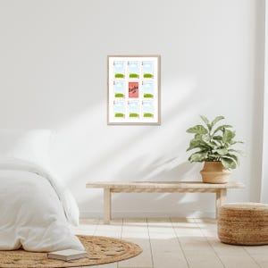 May include: A framed art print featuring a grid of twelve small images. Eleven images depict a green field and blue sky, while the central image has the text "Lucky us" on a pink background. The frame is light-colored.