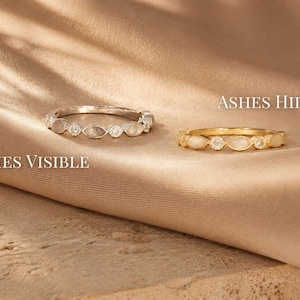 May include: Two rings, one silver and one gold, are displayed on a tan fabric. The silver ring, labeled "Ashes Visible," features alternating clear and opaque stones. The gold ring, labeled "Ashes Hidden," has a similar design. The text "Ashes Hidden" and "Ashes Visible" are also visible.