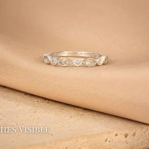 May include: A silver ring with alternating marquise-shaped and round clear stones. The ring is set against a tan fabric and a textured beige surface. The text "Ashes Visible" is at the bottom.