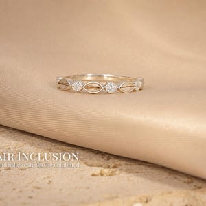 May include: A silver ring with a repeating pattern of oval shapes and small, round, clear stones. The ring is set against a beige fabric background. The text "HAIR INCLUSION" and "Hair and ashes can also be combined" is visible.