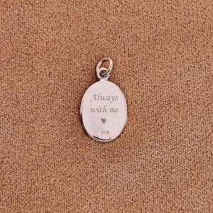 May include: Oval silver pendant with a loop at the top. The pendant is engraved with the words "Always with me" and a small heart. The pendant is on a brown textured surface.