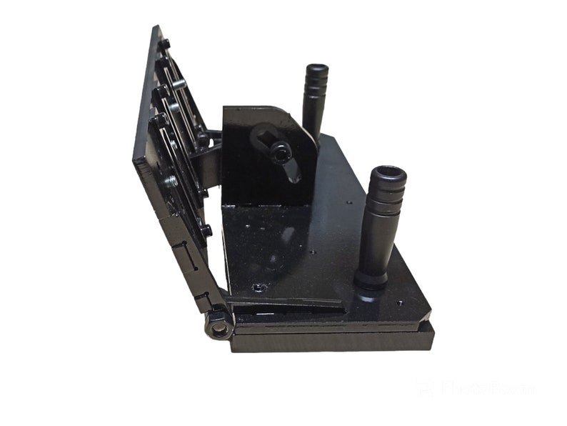 May include: A black metal tool with a hinged design. It features two vertical handles and a series of adjustable plates. The tool is designed for a specific mechanical purpose, with visible bolts and fasteners.