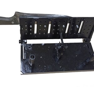 May include: A black metal knife sharpening jig with multiple adjustable slots and a handle. The jig is designed to hold a knife at a consistent angle for sharpening. The handle of the knife is visible on the left side of the image.