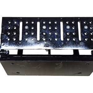 May include: A black metal adjustable platform with multiple holes and slots. The platform has a rectangular base and a top section with a series of evenly spaced holes and slots. The platform is designed to be adjustable and is likely used for industrial or mechanical purposes.