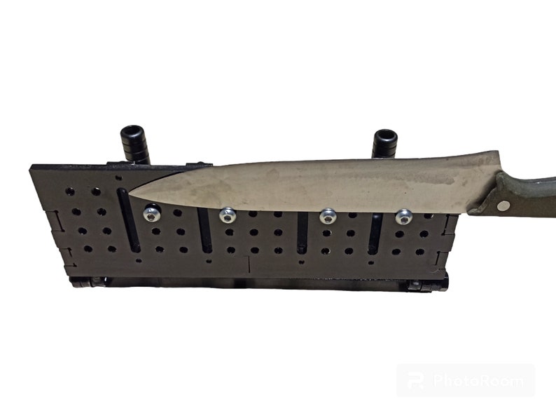 May include: A black knife sharpening system with a stainless steel knife in place. The system has multiple holes and slots, with silver bolts securing the knife. The knife has a green handle and a silver blade.
