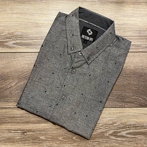May include: A gray button-down shirt with a small black pattern. The shirt has a collar and a button-up front. The shirt has a label that says "Pattern Ups" on it.