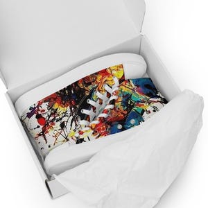 May include: High-top canvas sneakers with a vibrant abstract design in a white box. The sneakers feature a colorful splatter pattern with red, yellow, blue, and black hues. White laces and soles complete the design, offering a bold and artistic statement.