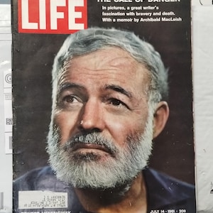 Pode incluir: Uma edição vintage da revista LIFE de 14 de julho de 1961 com um retrato de Ernest Hemingway na capa. A manchete diz THE CALL OF DANGER, com texto mencionando um livro de memórias de Archibald MacLeish. A capa exibe uma etiqueta de envio.