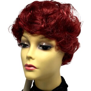 May include: A short, curly wig in a deep, vibrant red color displayed on a mannequin head. The hair features a textured, layered cut with voluminous curls that frame the face. The mannequin has a pale complexion, dark eyelashes, and pink lips.