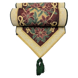 May include: A rolled-up burgundy and gold table runner with a poinsettia design. The runner features a repeating pattern of red poinsettias, green leaves, and gold accents. A green tassel hangs from the pointed end.