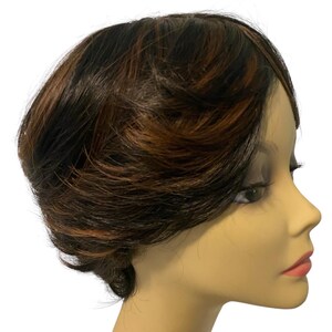 May include: A short, layered wig featuring a blend of dark brown and auburn highlights. The hair is styled in a textured, cropped cut that sits on a mannequin head, showcasing a side profile view with visible volume and varied color tones.