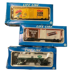 May include: Three vintage Life-Like model train cars in their original blue boxes. One is yellow with "Kellogg's Corn Flakes" text, another is white and brown with "Tootsie Roll" text, and the third is white and green with "Chemicals" text.