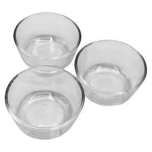 May include: Three clear glass bowls arranged in a group. The bowls are round with a slightly flared rim and a flat base. The glass is transparent, allowing a view through the bowls.