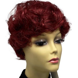 May include: A short, curly wig in a deep burgundy color. The wig is styled in a classic, layered cut. The wig is displayed on a mannequin head with a neutral skin tone, and the background is white.