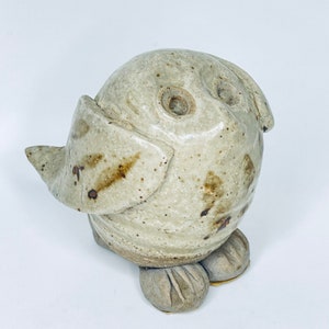 May include: A ceramic owl figurine with a white glaze and brown speckles. The owl has large eyes and small feet.