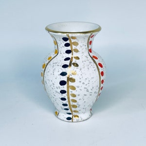 Könnte beinhalten: Eine weiße Keramikvase mit gesprenkeltem Finish und goldenen, schwarzen, roten und gelben bemalten Designs.