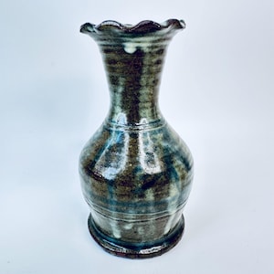 Peut inclure: Un vase en céramique fait à la main avec un bord festonné. Le vase présente une base marron foncé qui se transforme en un corps vert et bleu moucheté. Le vase a un col fin et un dessus évasé et décoratif. Le vase mesure environ 25 cm de haut.