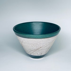 May include: A green and white ceramic bowl with a textured surface. The bowl is wide at the top and narrows to a point at the bottom.