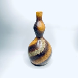 May include: A ceramic vase with a gourd-like form. The vase displays a mix of brown, tan, and beige hues in a swirling design. It has a slender neck and a rounded base. The overall aesthetic is rustic and earthy, with a height of approximately 25 cm.