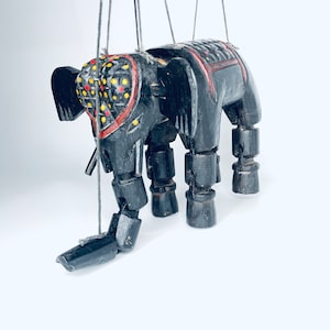 May include: A black wooden elephant puppet with red, yellow, and white painted details. The puppet has jointed legs and a long trunk.